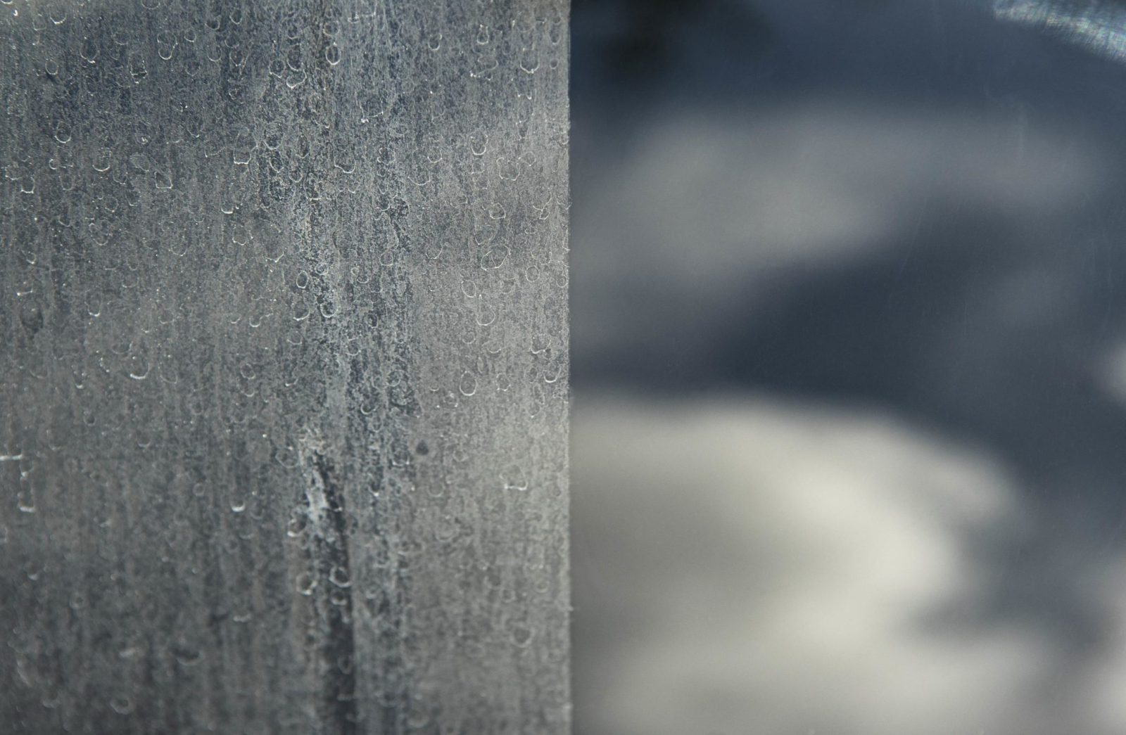 Close-up van een ruit: links vol opgedroogde spatten van gevelimpregnatie, rechts helder glas